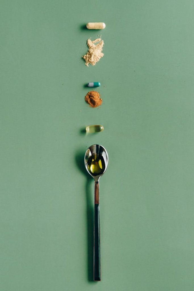 Assorted supplements and a spoon laid out on a green surface, showcasing health concepts.